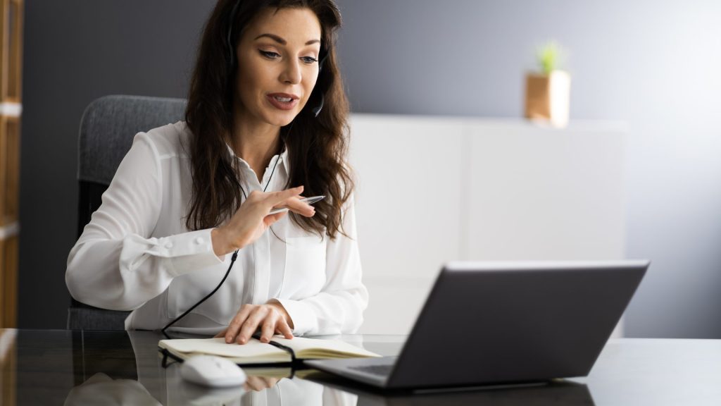 virtual-assistant-participating-in-a-meeting-while-using-a-laptop-and-taking-notes-in-a-notebook
