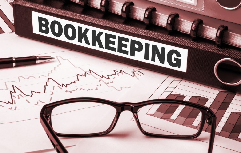 a-binder-with-the-word-bookkeeping-written-on-it-the-binder-is-sitting-on-a-table-with-a-pen-and-a-pair-of-black-glasses-with-a-white-rim-the-binder-is-closed