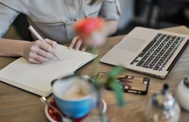 virtual-content-writer-working-on-laptop-with-notebook-pen-and-coffee-nearby-while-using-phone-for-research-and-writing
